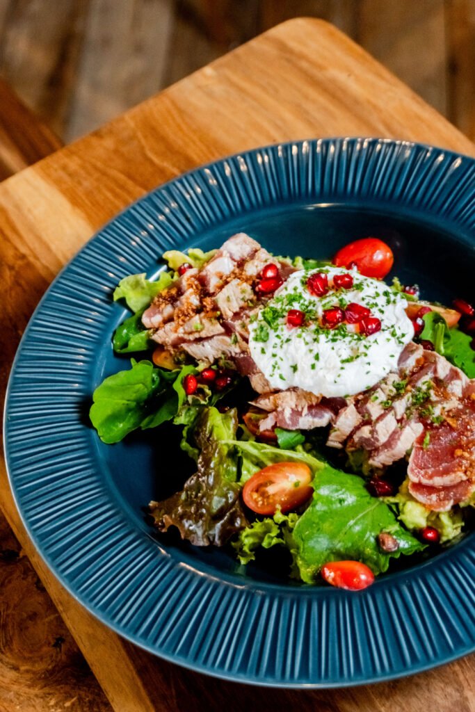Seared tuna salad with greens and pomegranate on a blue plate and wooden table